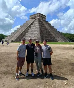 A pair of tourists smiling in front of the Pyramid of Kukulkan